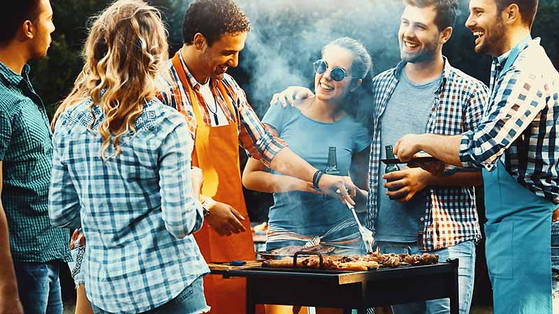 vrienden staan samen rondom een bbq te barbecueën